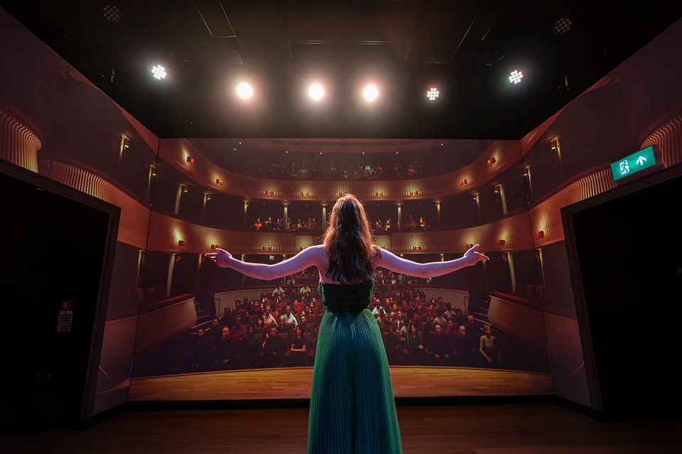A female student in a long green dress performing to a virtual audience in the RCM Performance Laboratory.